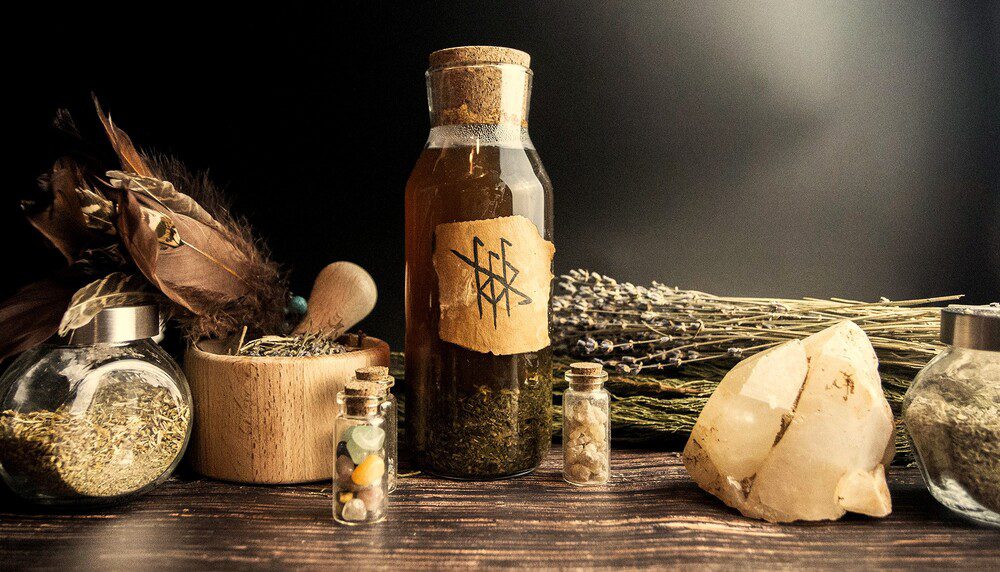 Apothecary bottles, dried herbs, and a crystal on a dark table, representing pattern clearing and foundational energy work