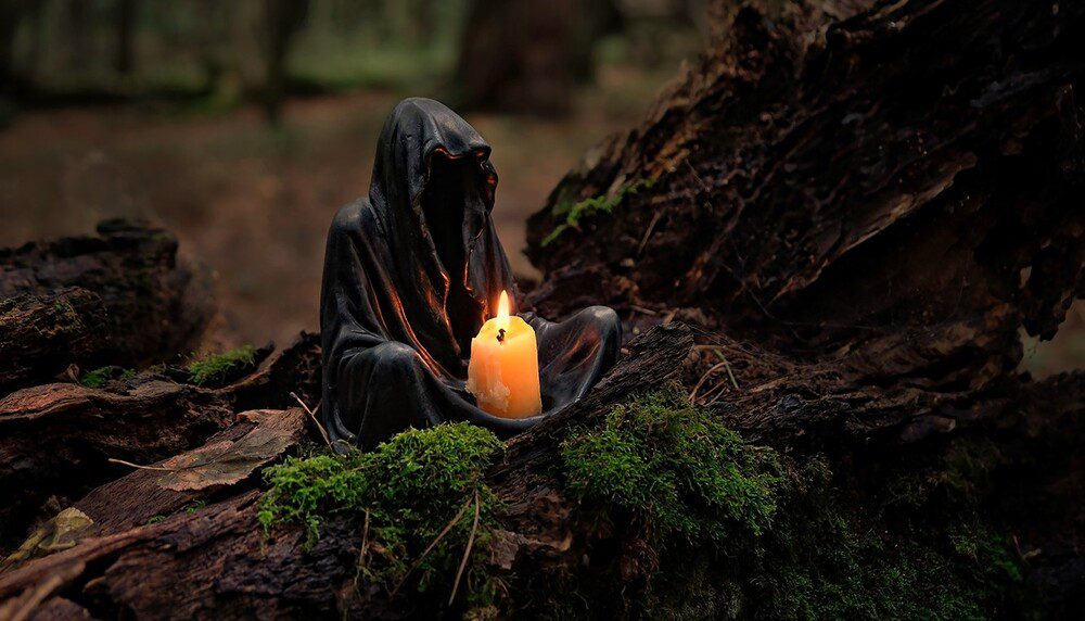 Hooded figure sitting in moss with a single lit candle, representing energetic crisis relief and calm presence
